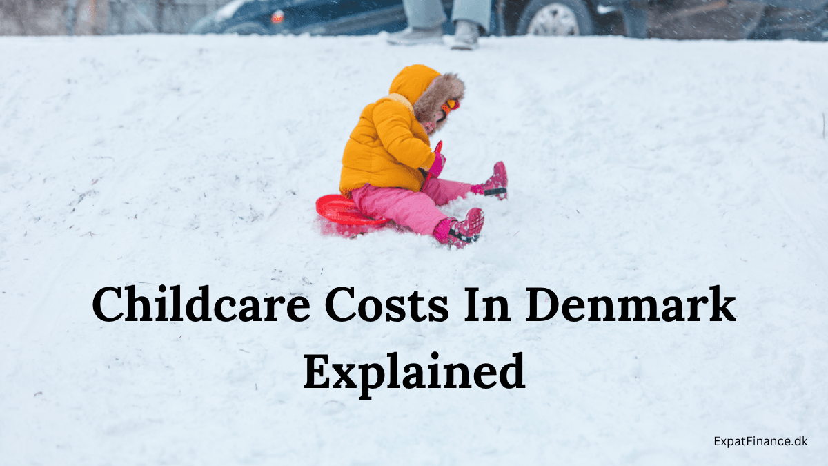 A young toddler wearing a bright yellow winter jacket and pink snowpants sledding down a snowy hill in Denmark, featuring the text overlay "Childcare Costs In Denmark Explained."