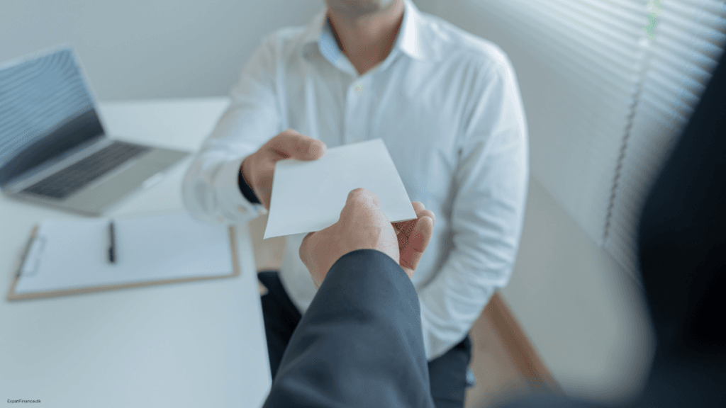 Hand handing a white envelope across an office desk next to a laptop, representing income differences between a freelancer and a traditional employee.