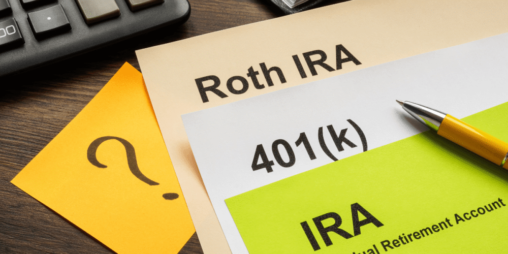 Roth IRA, 401(k), and IRA retirement account documents with a calculator and pen on a desk